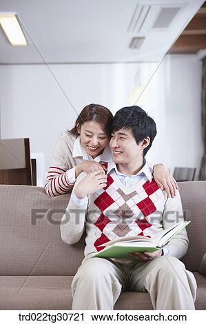 Stock Image - Happy couple with a man on the sofa with a book. Fotosearch
