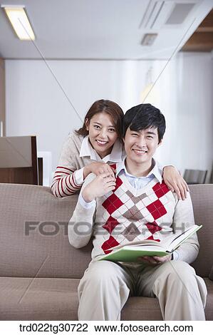 Stock Image - Happy couple with a man on the sofa with a book. Fotosearch