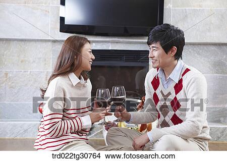 Picture - Happy couple with a wine in front of a fireplace. Fotosearch