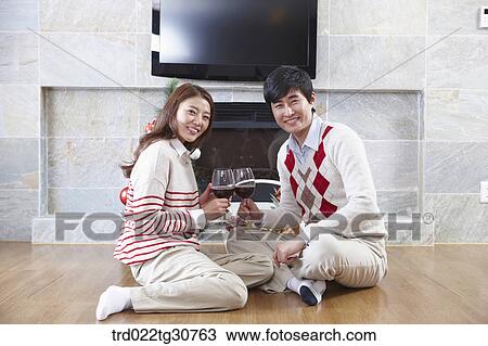 Stock Image - Happy couple with a wine in front of a fireplace. Fotosearch