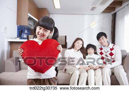 Stock Photography - Happy family and a girl holding a red heart cushion. Fotosearch