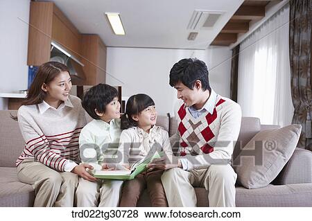 Stock Photo - Happy family talking with a book on the sofa. Fotosearch