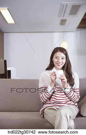 Stock Image - Happy woman with a cup on the sofa. Fotosearch