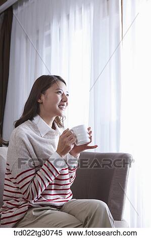 Stock Photography - Happy woman with a cup on the sofa. Fotosearch