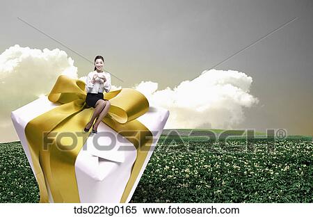 Stock Illustration - business woman is sitting on the gift box with coffee. Fotosearch