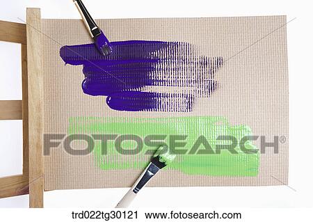 Stock Image - Blue and green paint with paintbrushes on easel. Fotosearch