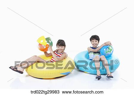 Stock Image - children holding beach balls and sitting on the tubes. Fotosearch