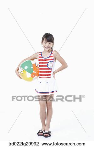 Stock Image - girl is standing with holding beach ball in her arm. Fotosearch