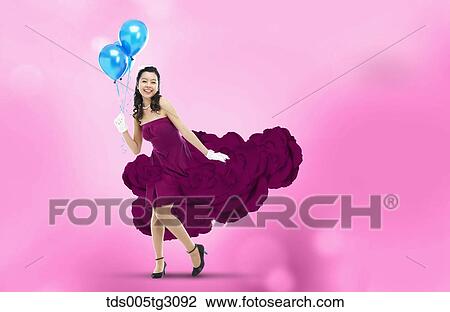 Stock Image - Woman Wearing Violet Flower Dress Holding Blue Balloons. Fotosearch