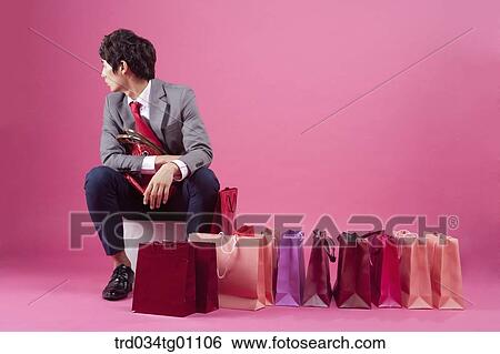 Stock Photograph - A bored man having a purse with many shopping bags around. Fotosearch