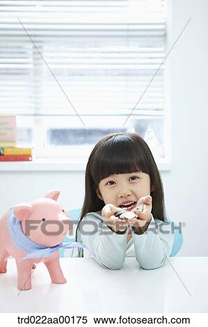 Stock Photography - A girl holding coin in her hands with a pink piggy bank . Fotosearch