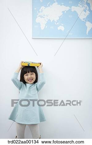 Picture - A girl holding up books over her head with the world map . Fotosearch