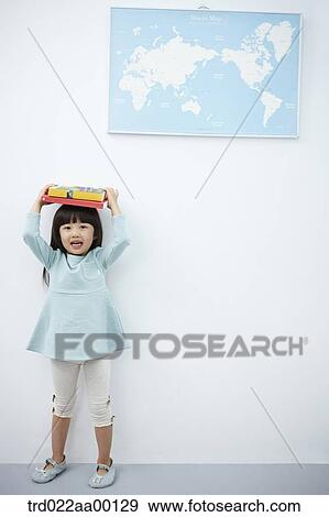 Stock Photo - A girl holding up books over her head with the world map . Fotosearch