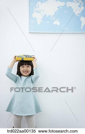 Stock Photography - A girl holding up books over her head with the world map . Fotosearch