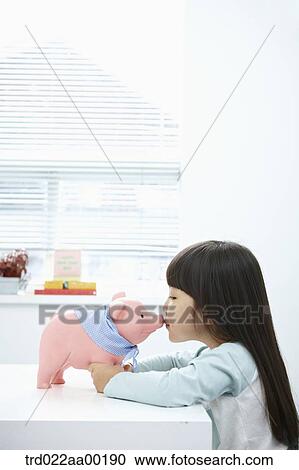 Stock Image - A girl kissing a pink piggy bank. Fotosearch