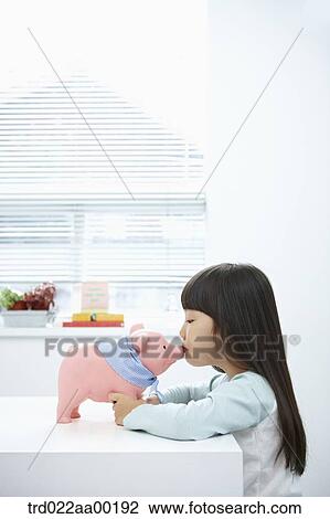 Stock Image - A girl kissing a pink piggy bank. Fotosearch