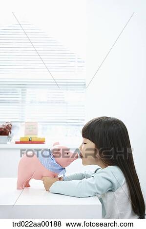 Stock Photo - A girl kissing a pink piggy bank. Fotosearch