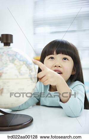 Stock Photo - A girl looking a globe with her hand pointing it. Fotosearch