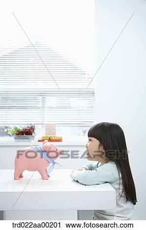 Stock Image - A girl looking at a pink piggy bank. Fotosearch