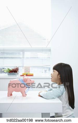 Stock Photo - A girl looking at a pink piggy bank. Fotosearch