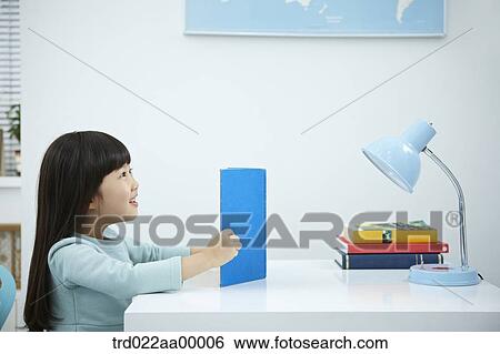 A girl reading a book in front of the desk View Large Photo Image Stock Photograph - A girl reading a book in front of the desk. Fotosearch