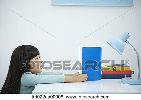 A girl reading a book in front of the desk View Large Photo Image Stock Photography - A girl reading a book in front of the desk. Fotosearch