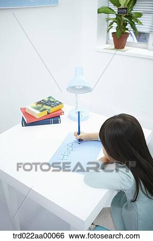 Stock Photograph - A girl writing 'Happy' on the blue paper with a blue colored pencil. Fotosearch