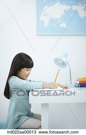 Stock Image - A girl writing on a book in front of the desk. Fotosearch