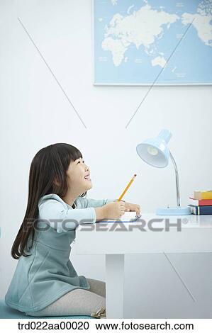 Stock Image - A girl writing on a book in front of the desk. Fotosearch