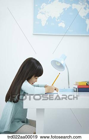 A girl writing on a book in front of the desk View Large Photo Image Stock Photo - A girl writing on a book in front of the desk. Fotosearch