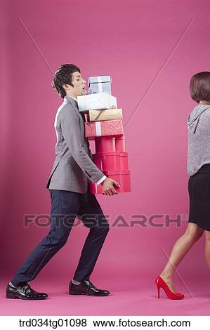 Stock Photo - A man following a woman with the piled gift boxes on his hand . Fotosearch