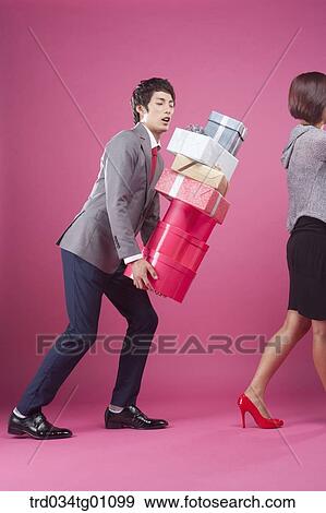 Stock Photo - A man following a woman with the piled gift boxes on his hand . Fotosearch