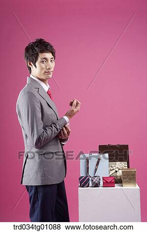 Stock Photo - A man having his button up beside the shopping bag and gift box. Fotosearch