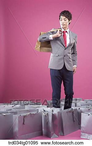 Stock Photography - A man holding up the gold colored shopping bag with other gray shopping bags around. Fotosearch