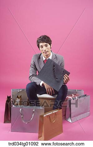 Stock Image - A man holding up the shopping bag with many shopping bags around. Fotosearch