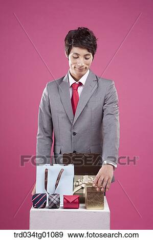 Stock Photo - A man looking down on the shopping bag, colorful tie, and gift box. Fotosearch