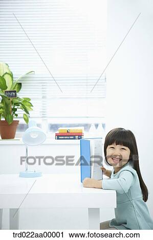 A smiling girl having a book in front of the desk View Large Photo Image Stock Image - A smiling girl having a book in front of the desk. Fotosearch