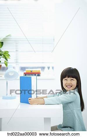 A smiling girl having a book in front of the desk View Large Photo Image Stock Image - A smiling girl having a book in front of the desk. Fotosearch