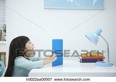 A smiling girl having a book in front of the desk View Large Photo Image Stock Photo - A smiling girl having a book in front of the desk. Fotosearch