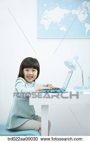 Stock Image - A smiling girl having her hands on keyboard of a laptop in front of the desk. Fotosearch