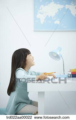 Stock Image - A smiling girl holding a pencil over a book. Fotosearch