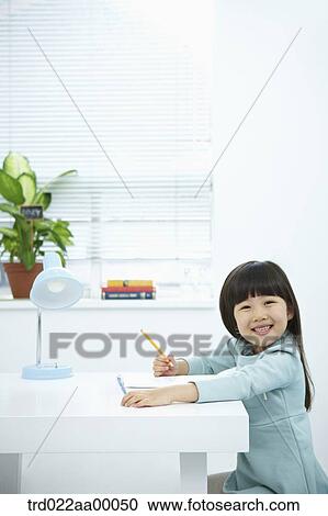 Stock Image - A smiling girl holding a pencil over a book. Fotosearch