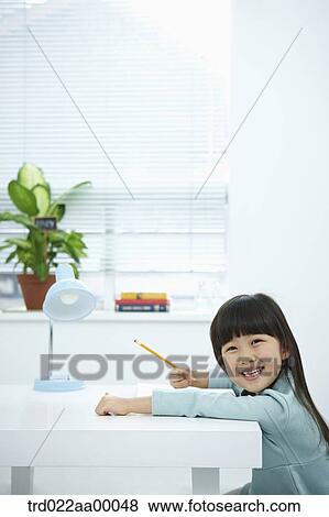 Stock Photo - A smiling girl holding a pencil over a book. Fotosearch
