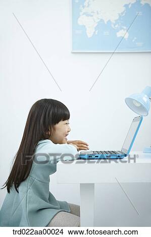 A smiling girl looking at a laptop in front of the desk View Large Photo Image Picture - A smiling girl looking at a laptop in front of the desk. Fotosearch