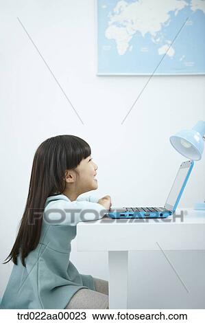 Stock Image - A smiling girl looking at a laptop in front of the desk. Fotosearch