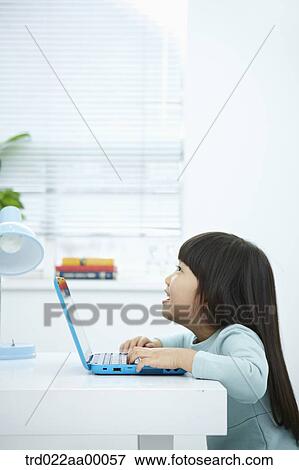 Stock Photo - A smiling girl looking at a laptop in front of the desk. Fotosearch