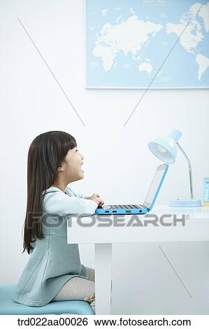 A smiling girl looking at a laptop in front of the desk View Large Photo Image Stock Photograph - A smiling girl looking at a laptop in front of the desk. Fotosearch