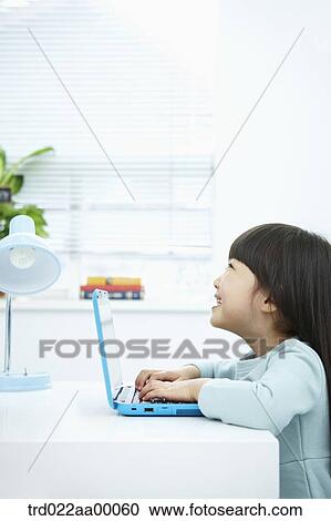 Stock Image - A smiling girl pushing the keyboard of a laptop in front of the desk. Fotosearch