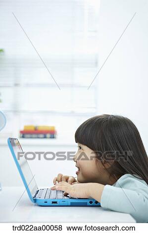 Stock Photo - A smiling girl pushing the keyboard of a laptop in front of the desk. Fotosearch