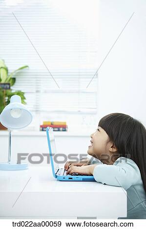 Stock Photo - A smiling girl pushing the keyboard of a laptop in front of the desk. Fotosearch